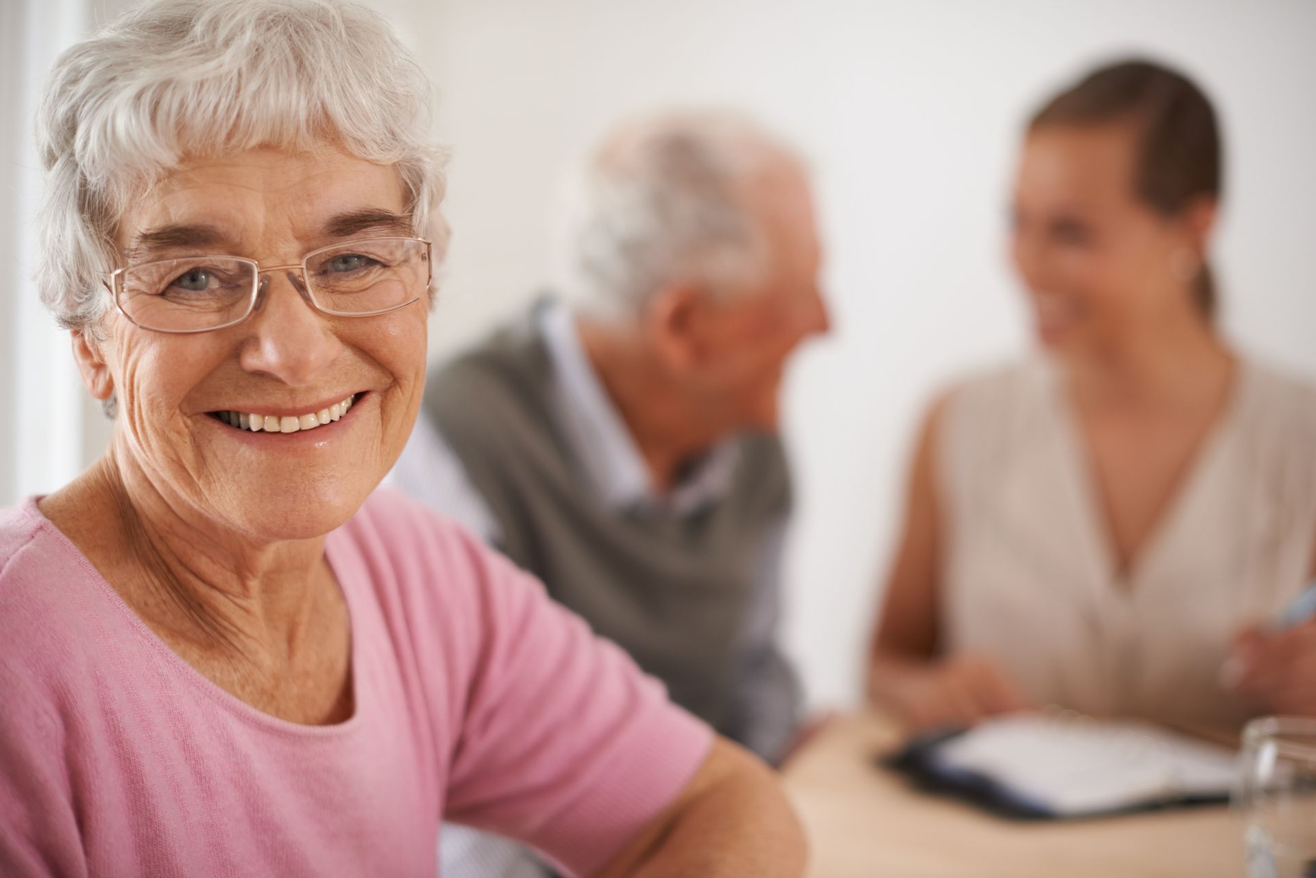Smiling woman with glasses, foreground; couple and person with clipboard in background.