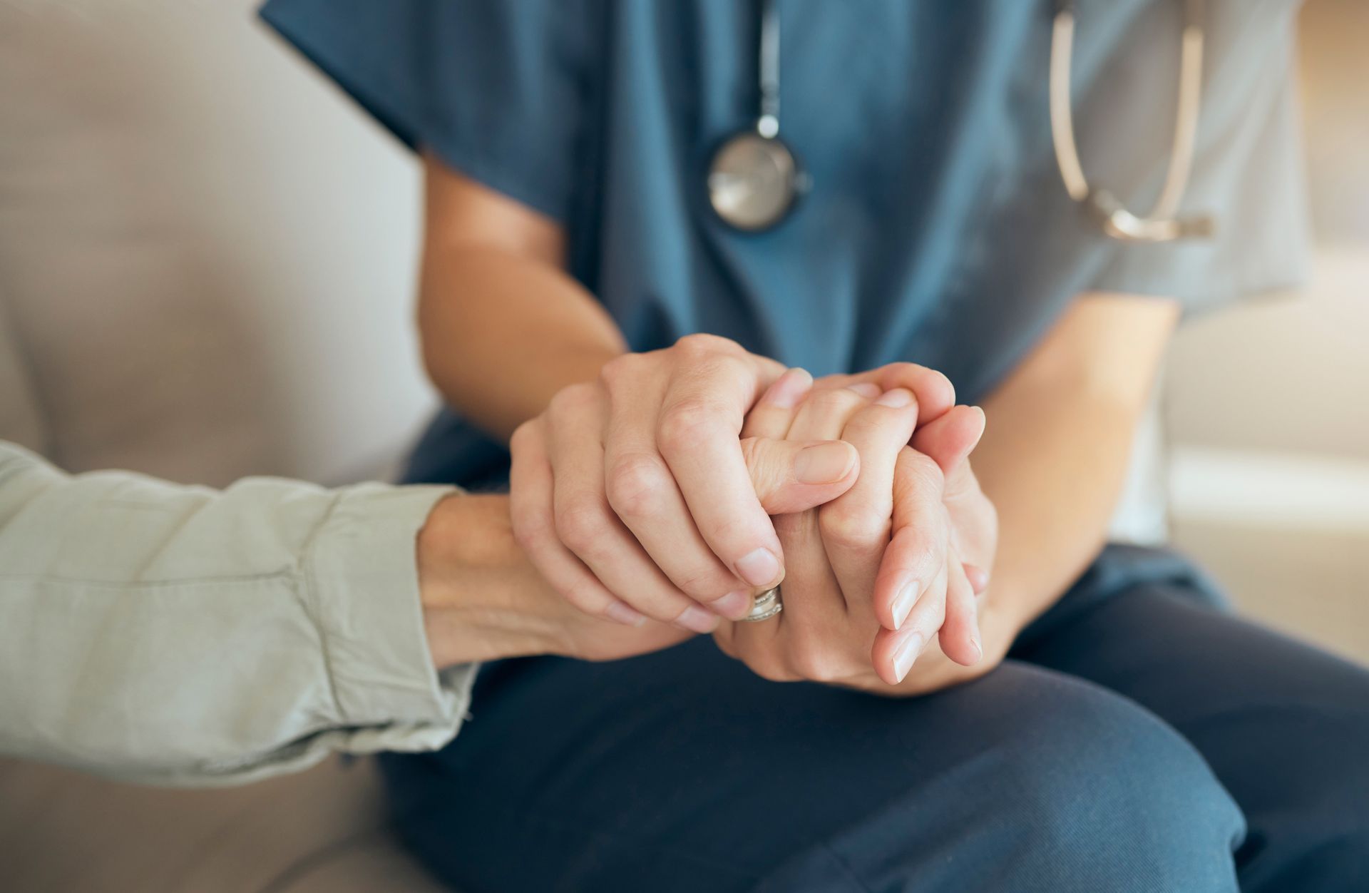 Person in blue scrubs holding hands with another person, offering support.