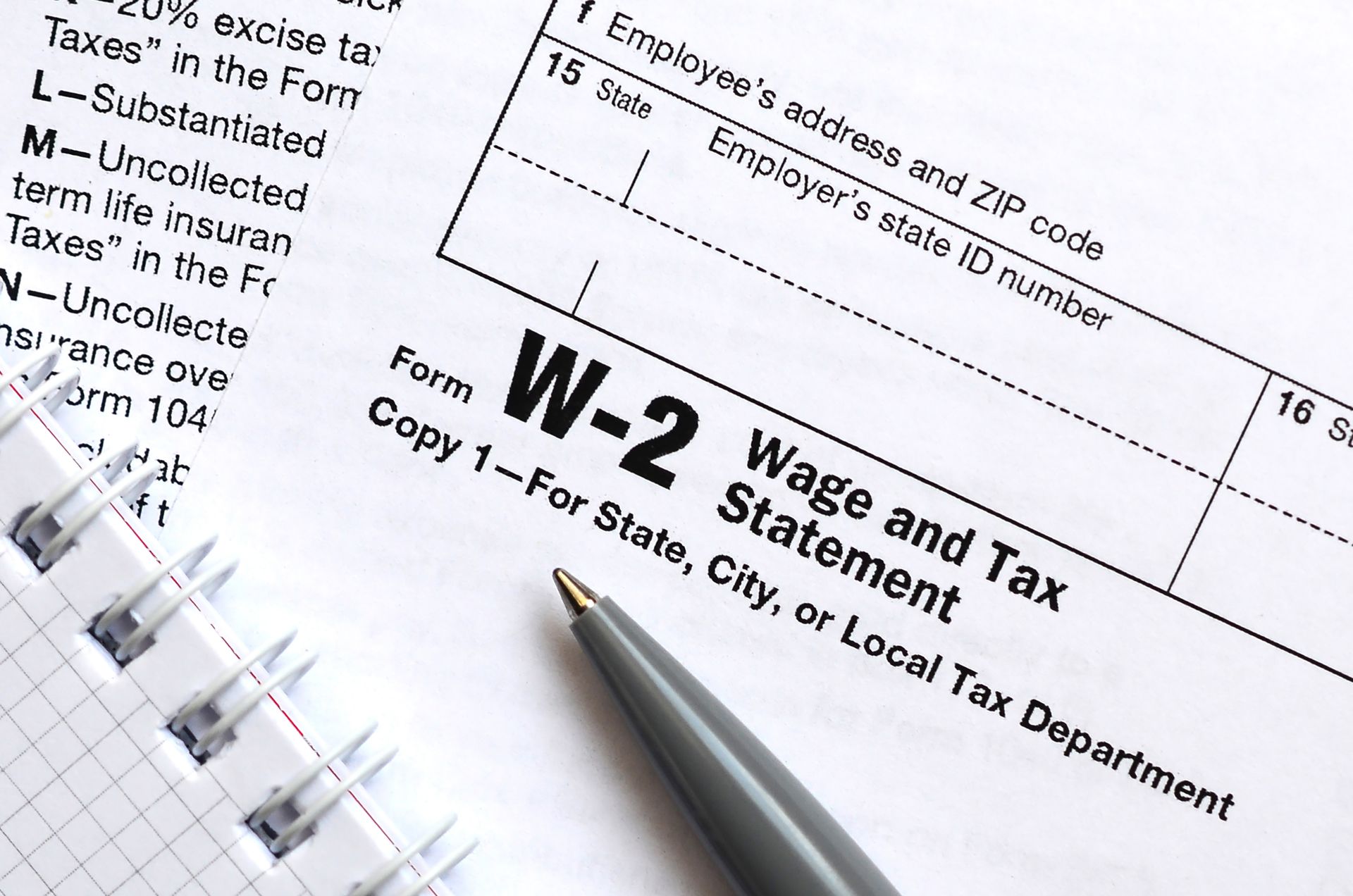 W-2 tax form with a pen resting on it; a notepad is in the background.