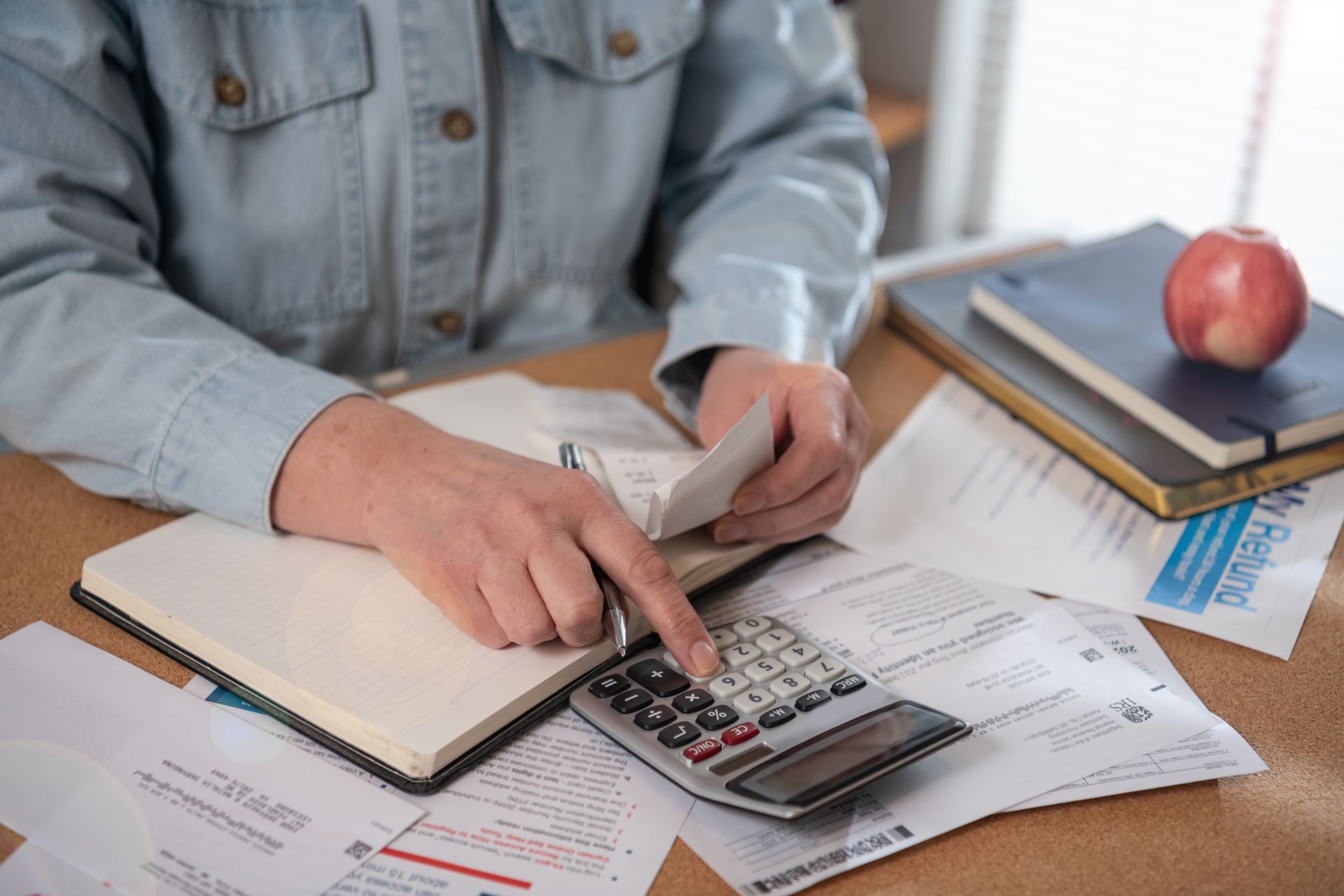 Person using a calculator, surrounded by bills and a notepad on a wooden table.