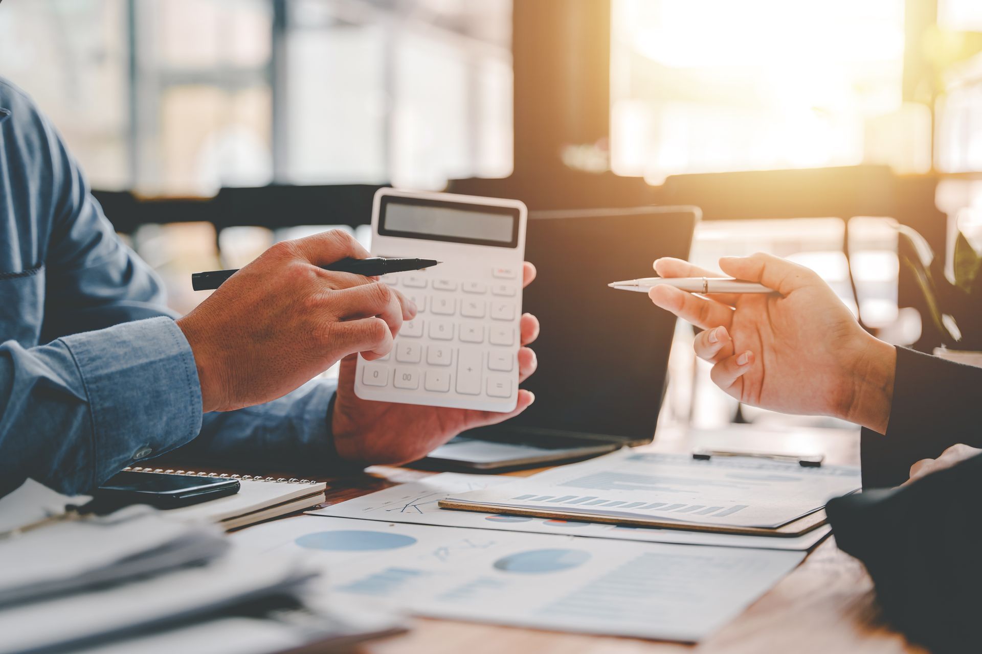 Two people reviewing financial data with calculator and documents on a table.
