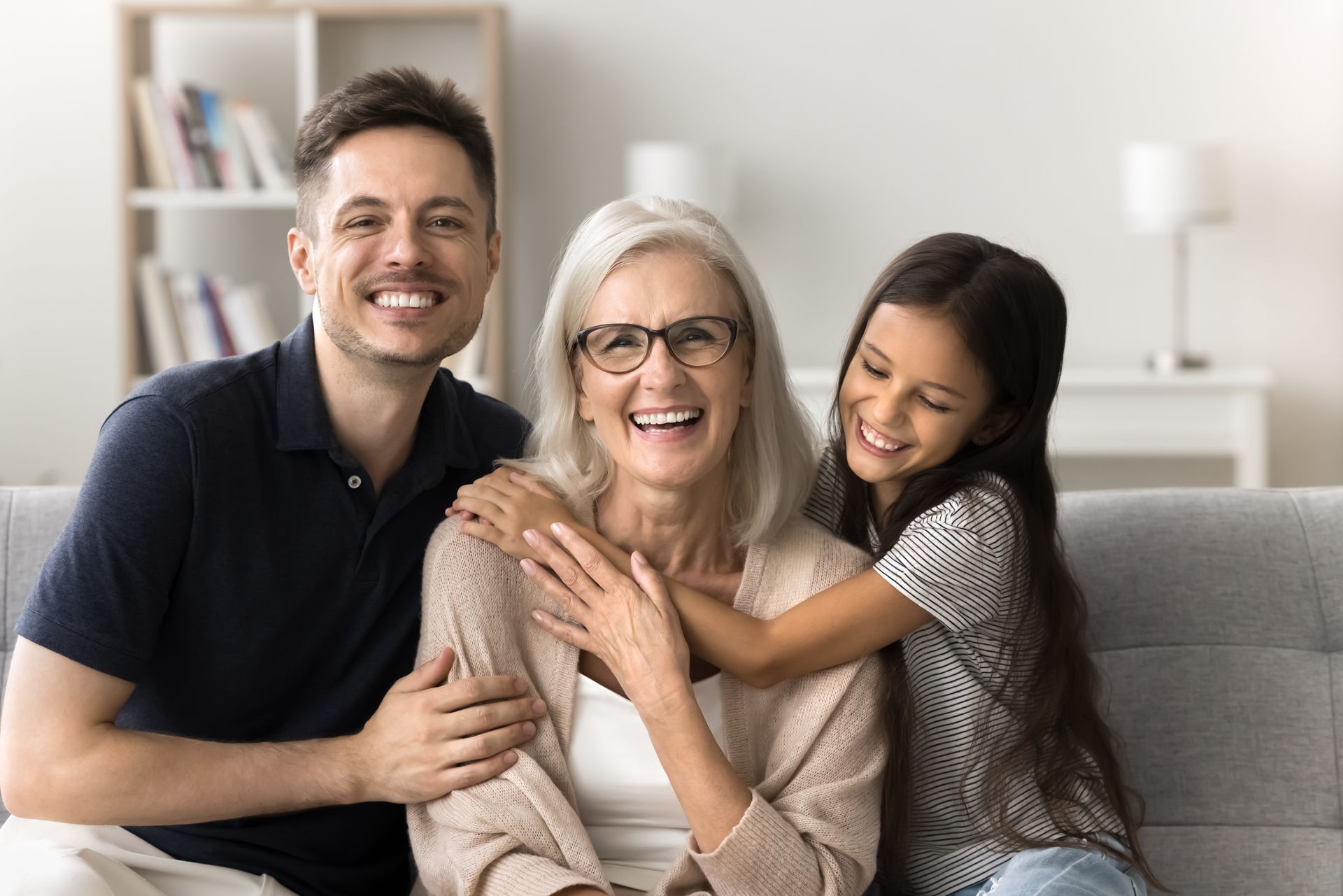 A family of three smiles for the camera on a gray couch in a living room.