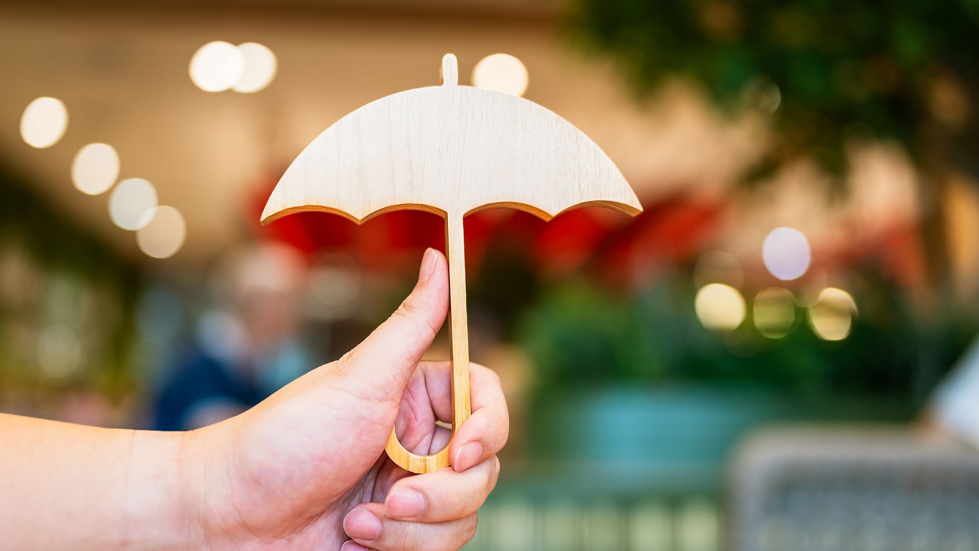Hand holding a small, light wooden umbrella against a blurred background.