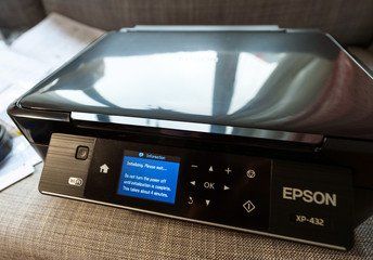 Uma impressora epson preta está em cima de um sofá.