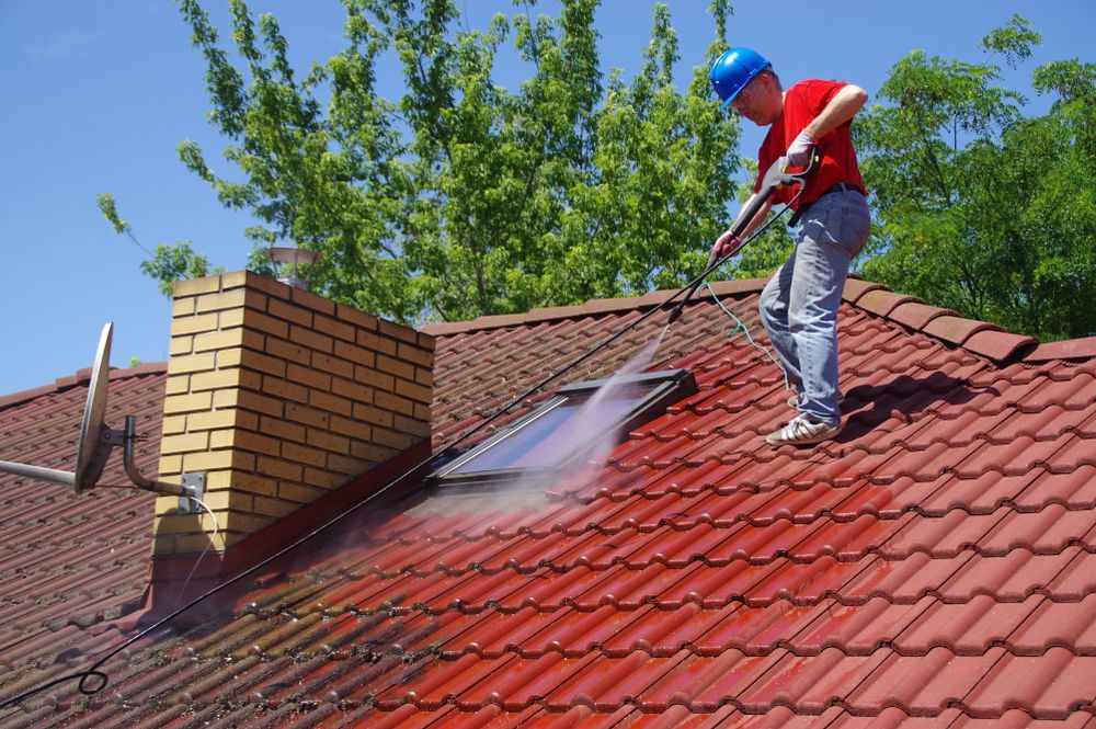 Man power washing a red tile roof, with a chimney and skylight visible.