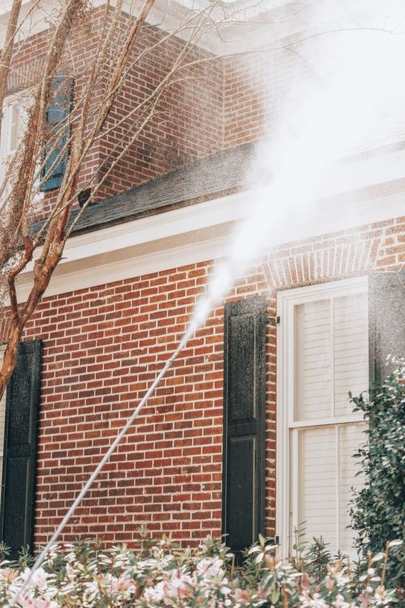 Pressure washing a brick building with black shutters and white trim.