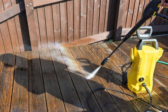 Yellow pressure washer spraying water on a wooden deck next to a brown wooden fence.