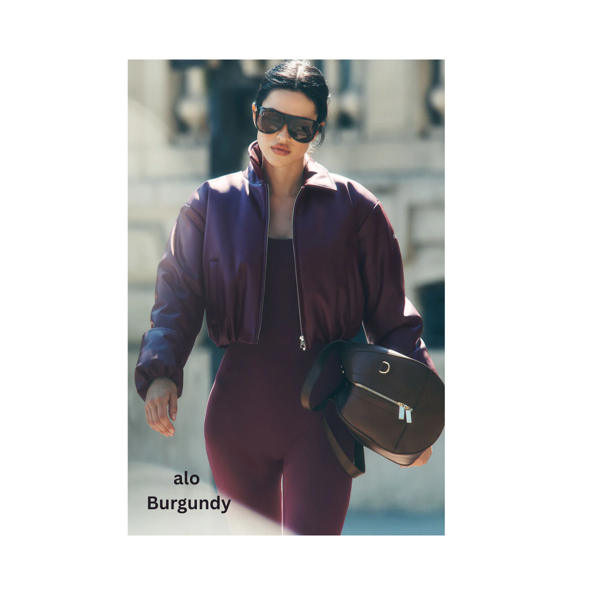 Woman in burgundy outfit walking, wearing sunglasses, carrying a bag.