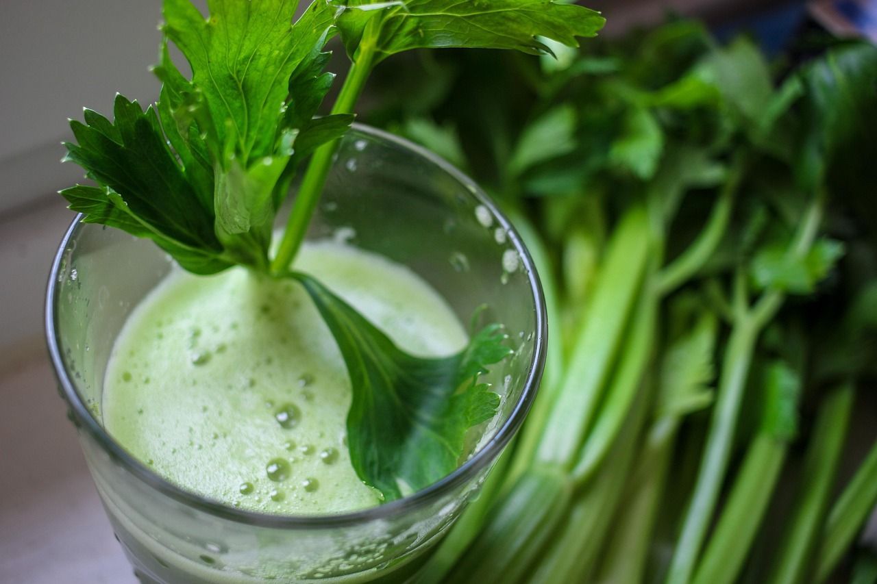 Glass of green celery juice, celery leaves garnish, bunch of celery stalks.
