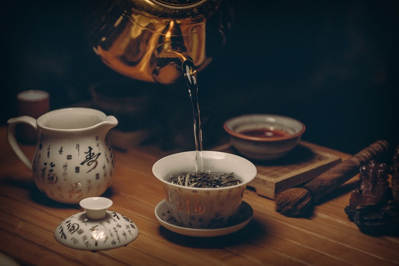 Water being poured from a golden kettle into a teacup, part of a tea ceremony setup.