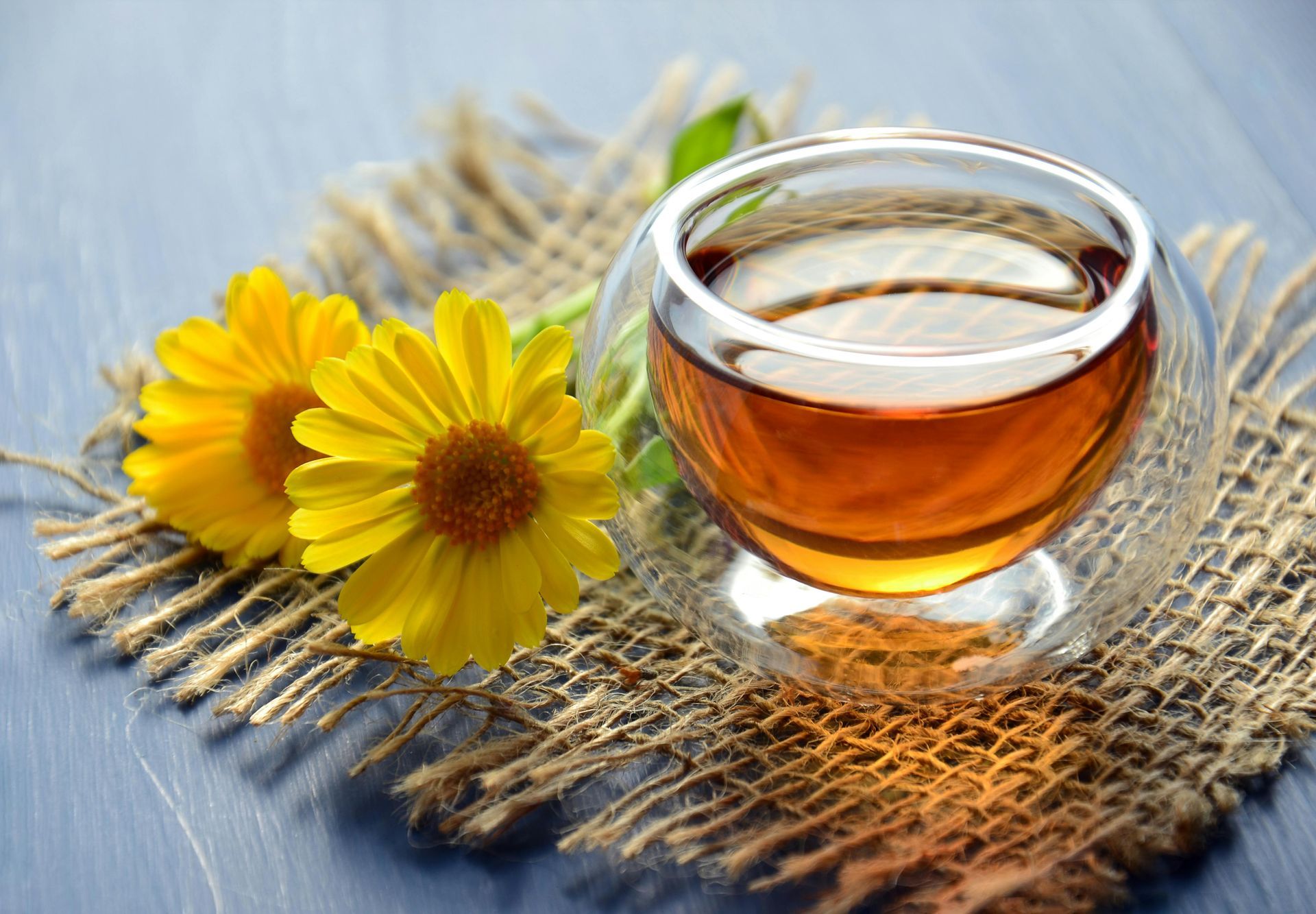 Glass of tea on burlap with two yellow flowers.