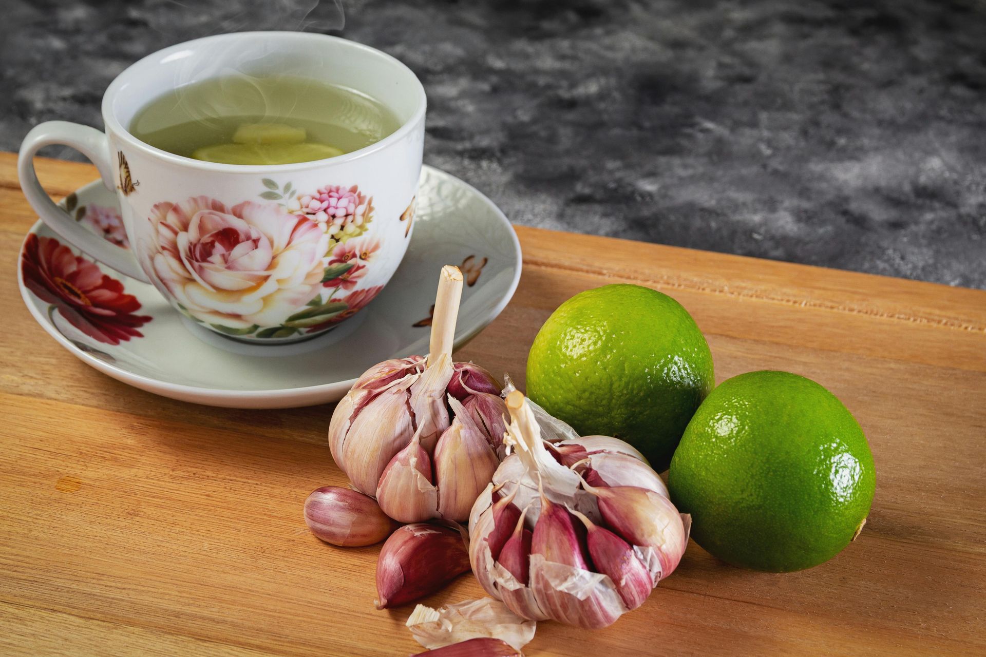 Cup of tea with garlic cloves and limes on a wooden board.