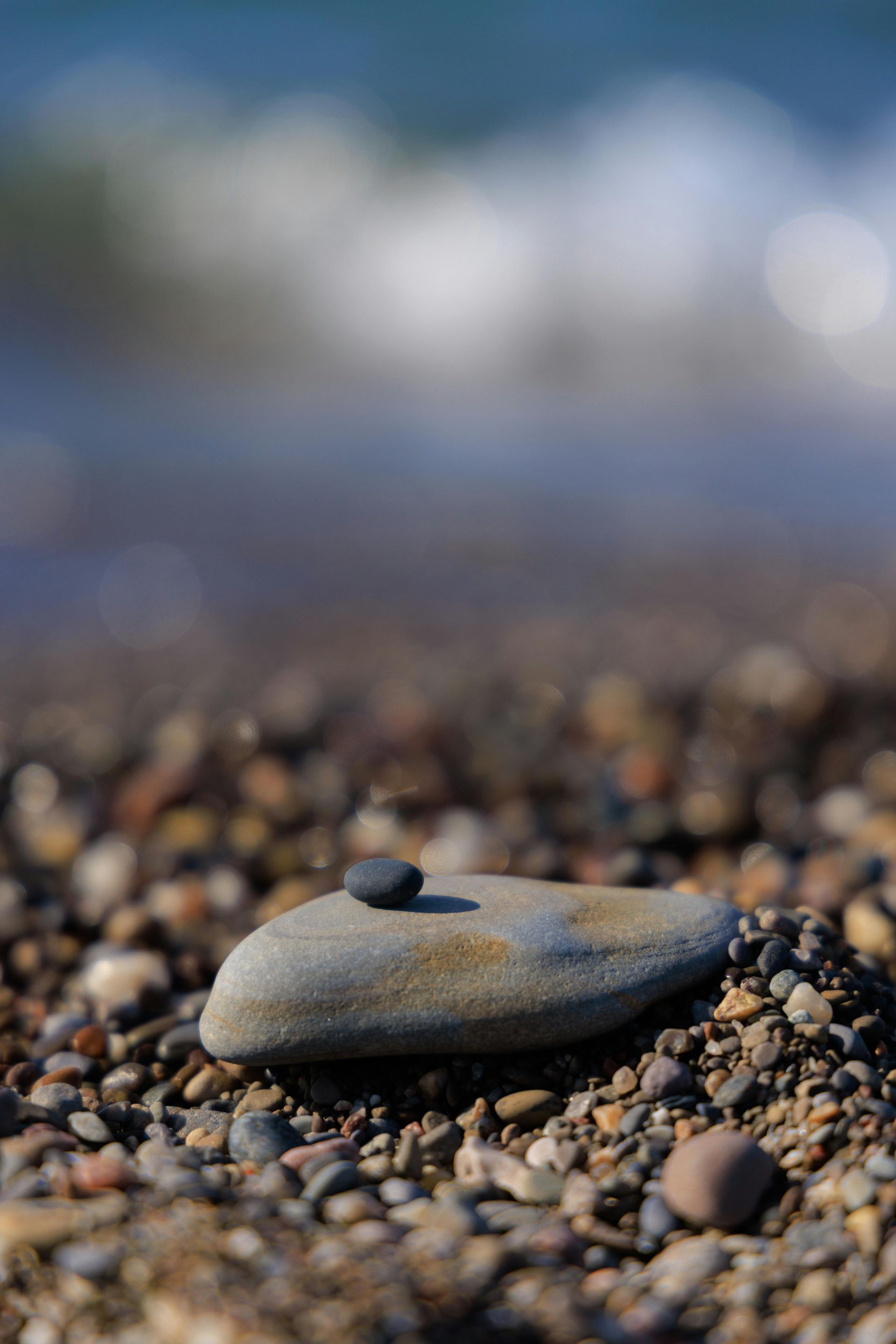 Two stones stacked on a pebble beach with the ocean in the background.