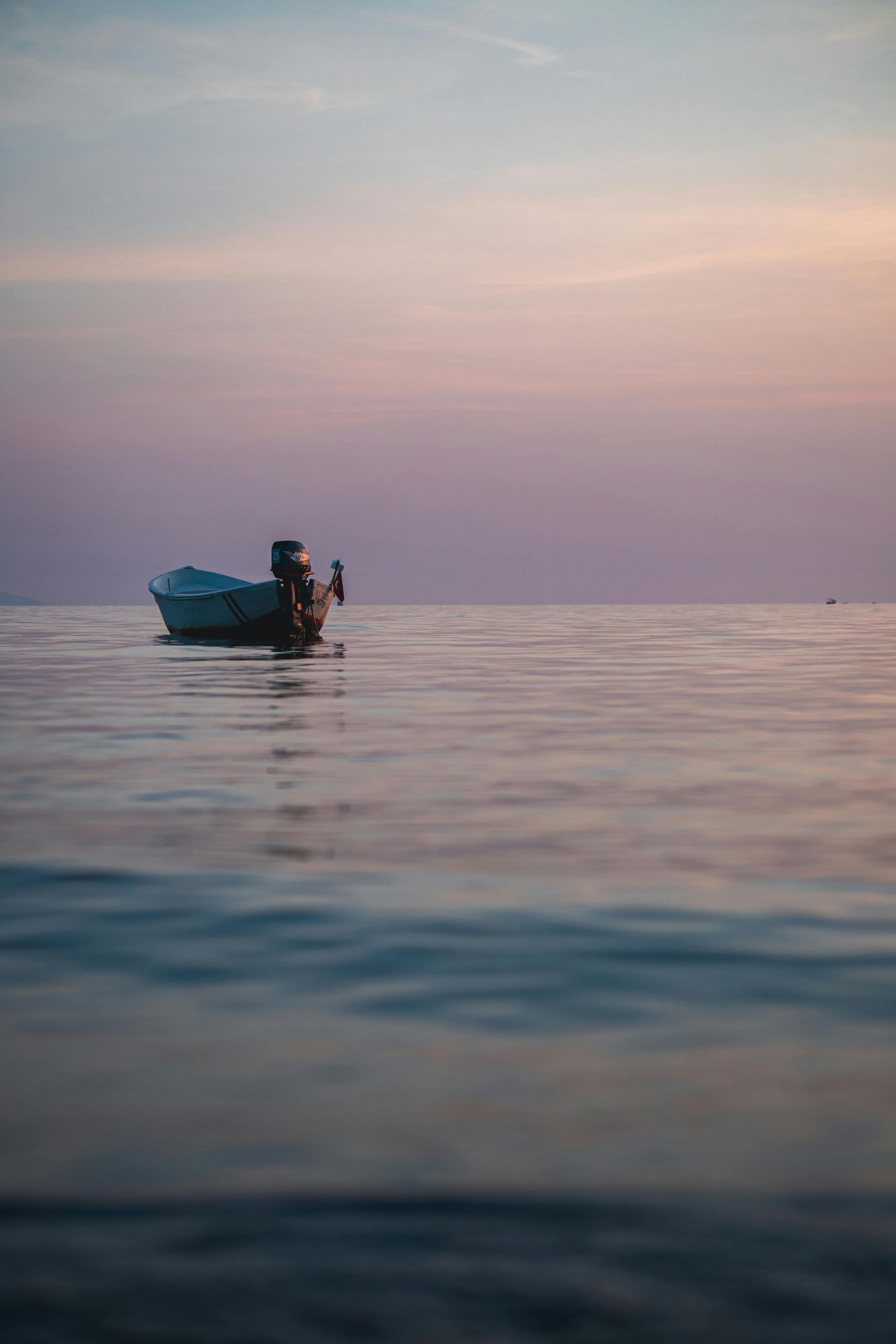 Boat floating on calm water at sunset, purple and blue hues in the sky.
