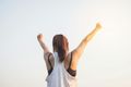 Woman with arms raised in victory, set against a bright, clear sky.