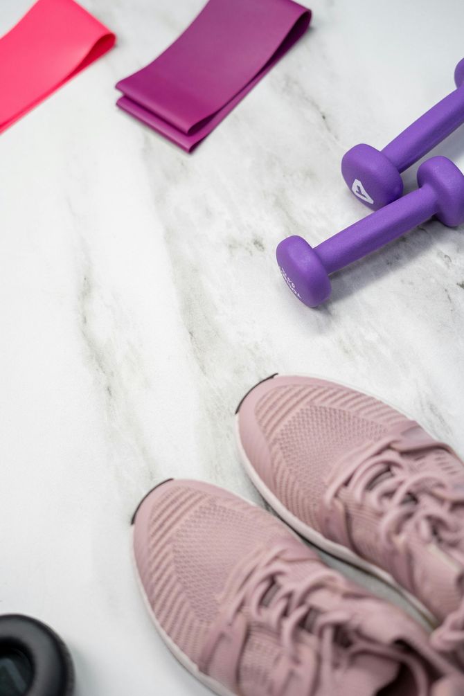 Pink sneakers, purple dumbbells, and resistance bands on a marble surface, ready for a workout.