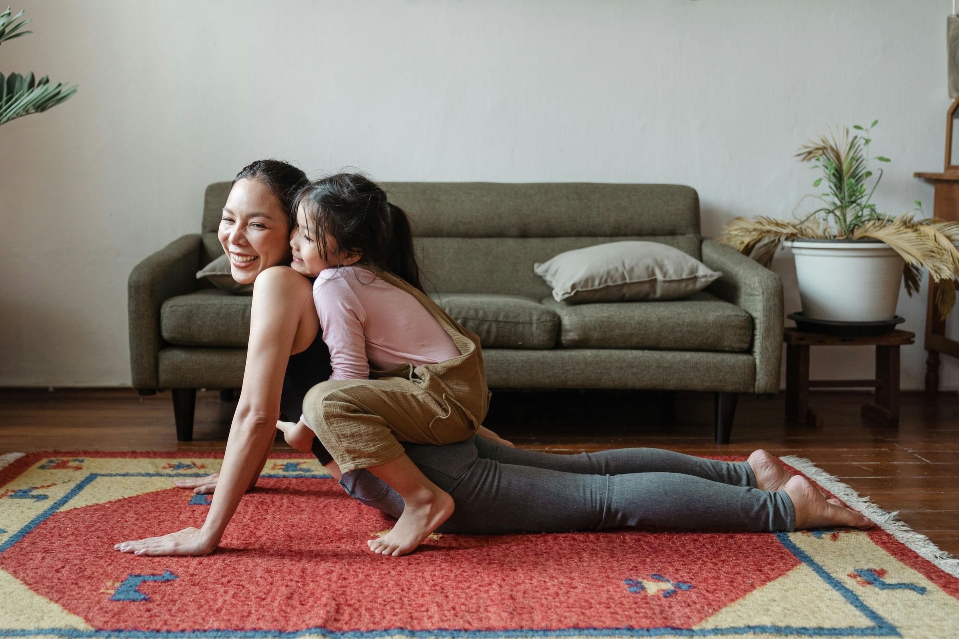 Woman doing yoga with child on her back on a red rug in a living room.