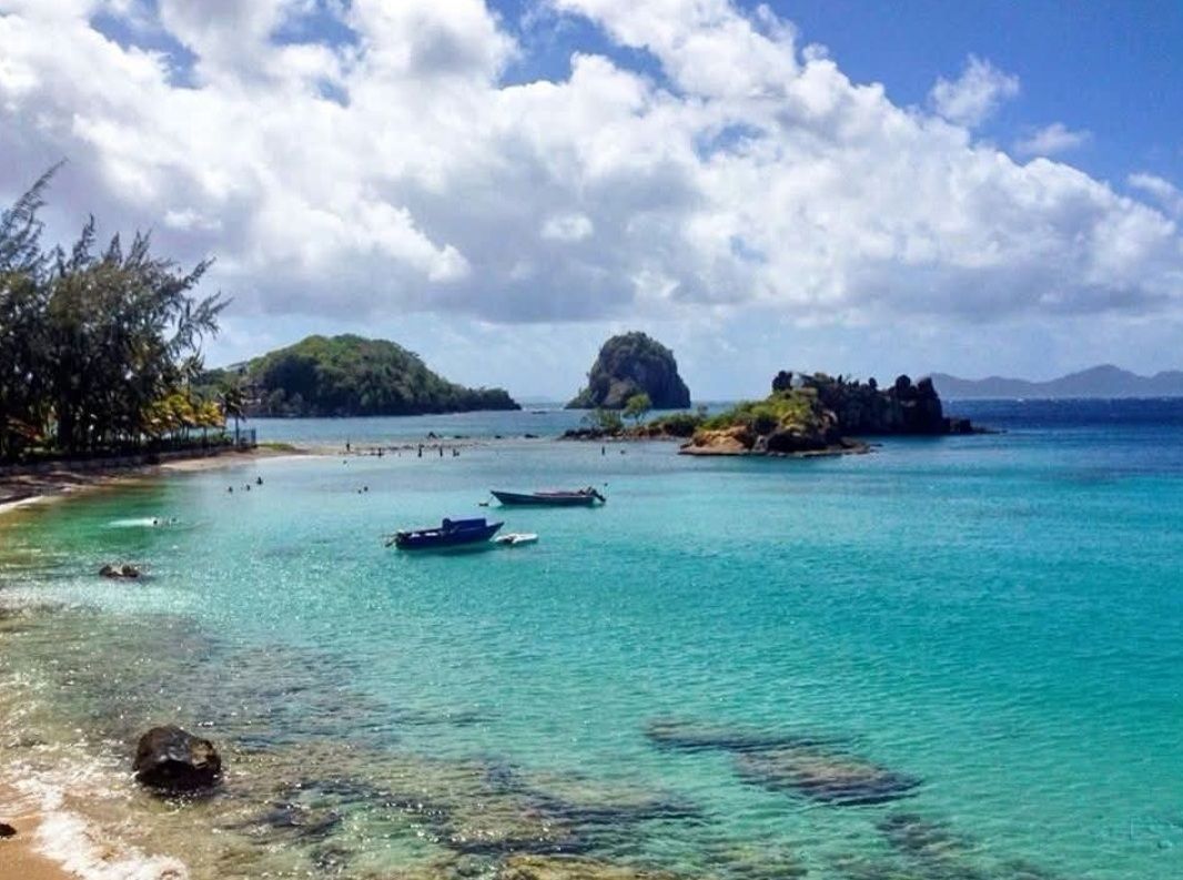 Turquoise ocean view with boats, islands, and a beach under a blue sky with white clouds.