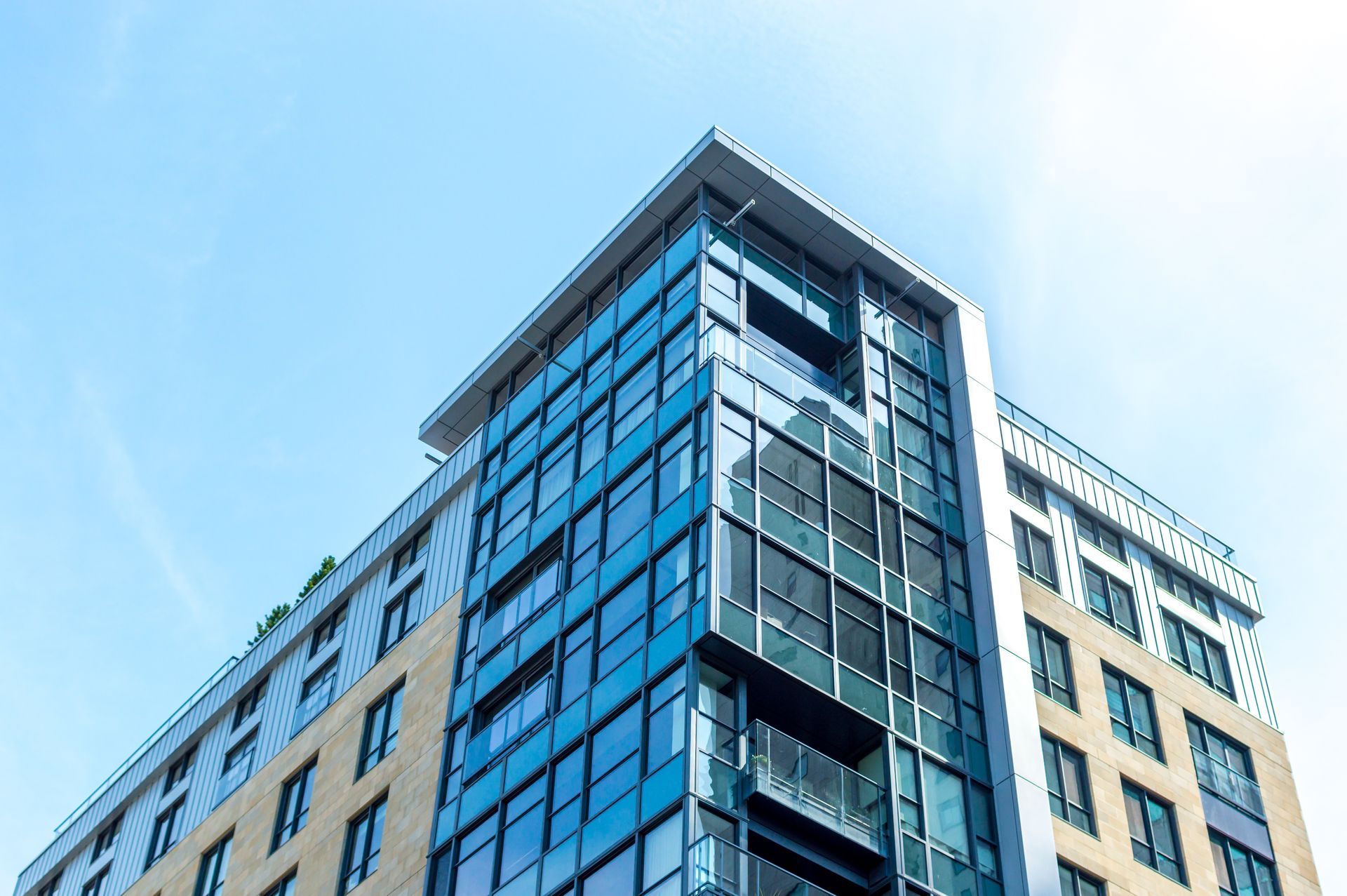Immeuble d'appartements moderne de grande hauteur avec verre bleu et extérieur beige, sur fond de ciel bleu vif.