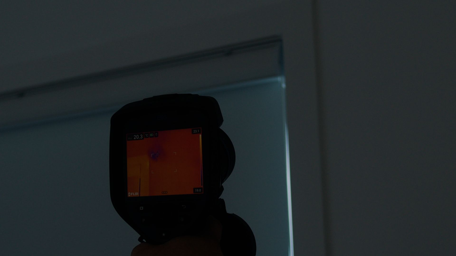 Une personne tient une caméra thermique dans sa main dans une pièce sombre.