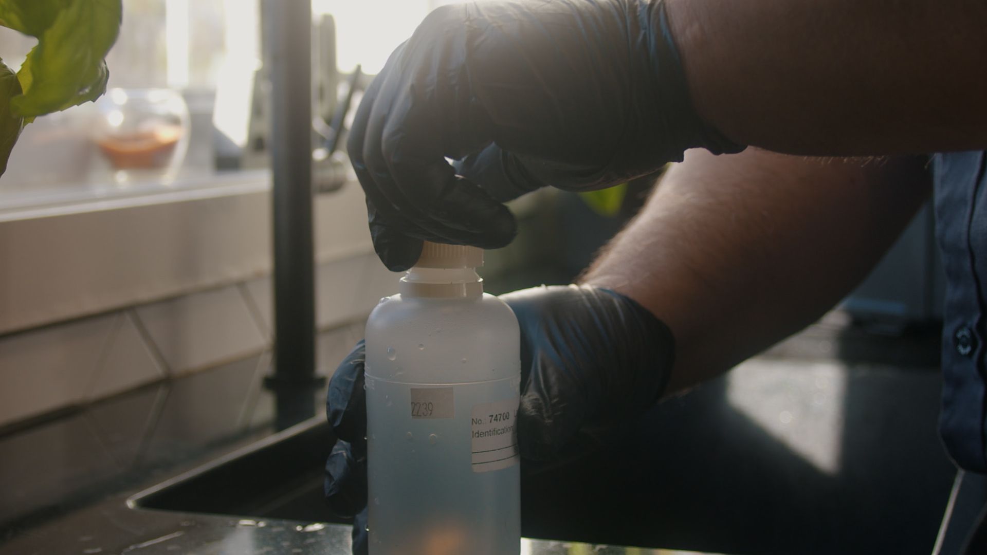 Une personne portant des gants noirs verse de l'eau dans une bouteille.