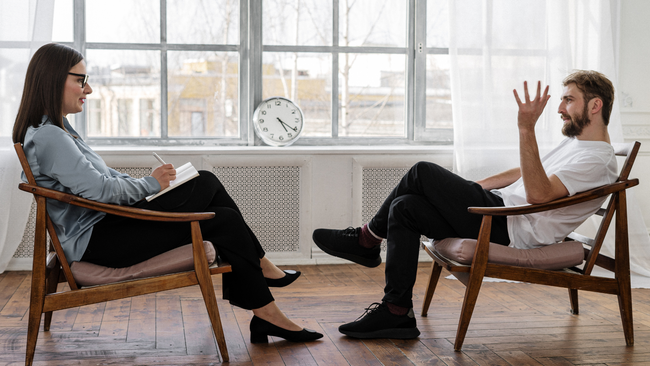 A man is sitting at a table with a clipboard in front of a couple sitting on a couch.