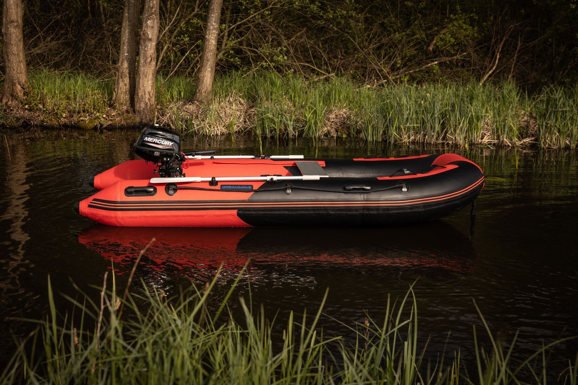Een rood-zwarte boot met motor drijft op een rivier.