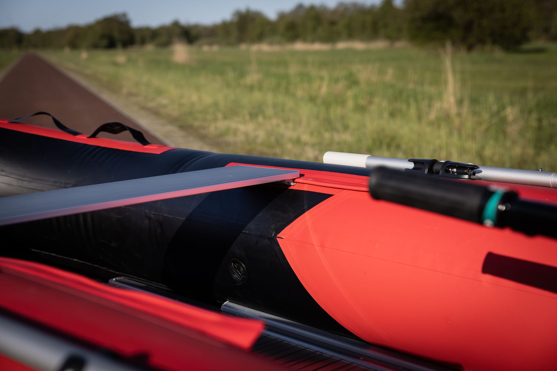 Een rode en zwarte opblaasbare boot met roeiriemen zit in een veld.