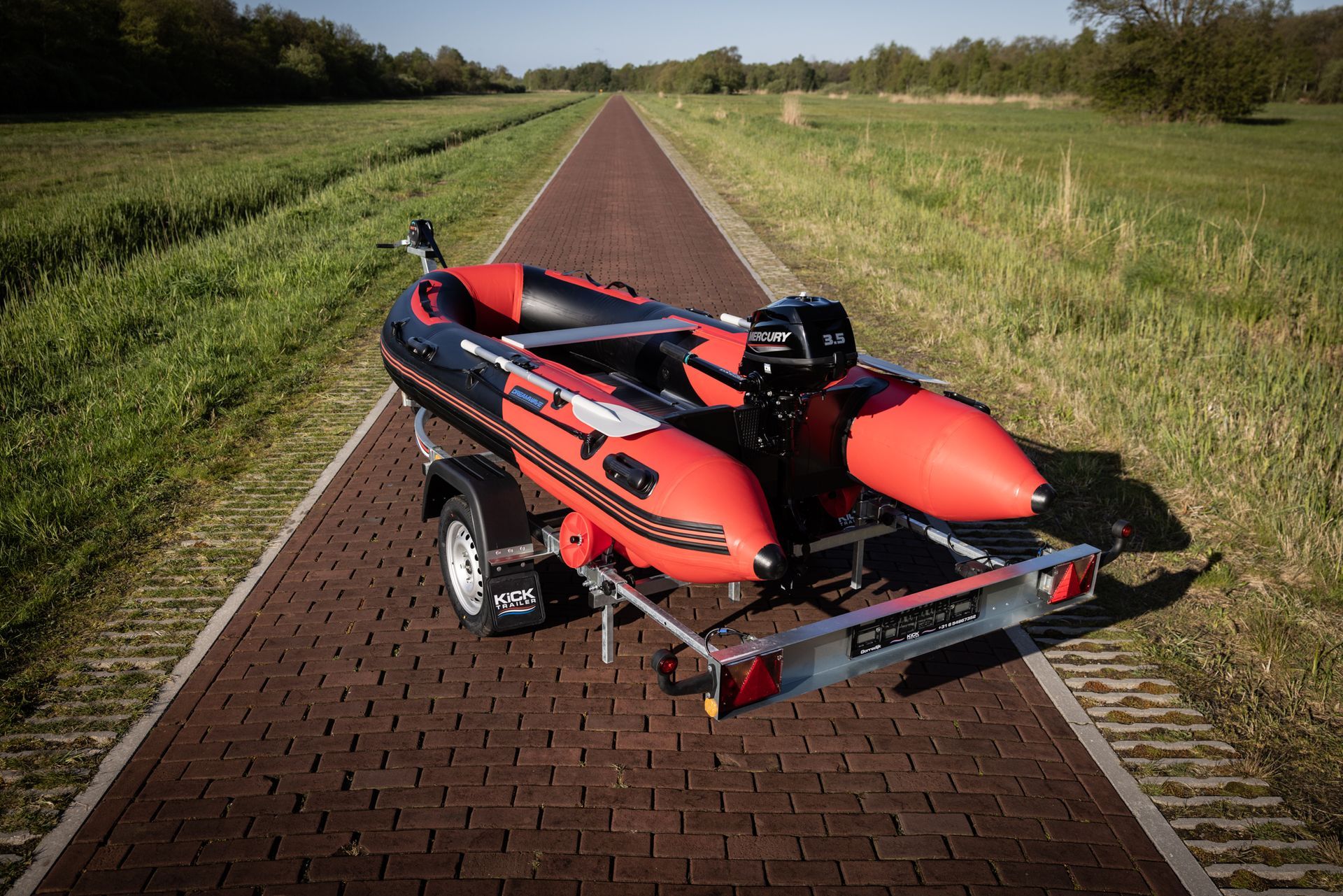 Een rode boot staat op een trailer op een stenen weg.