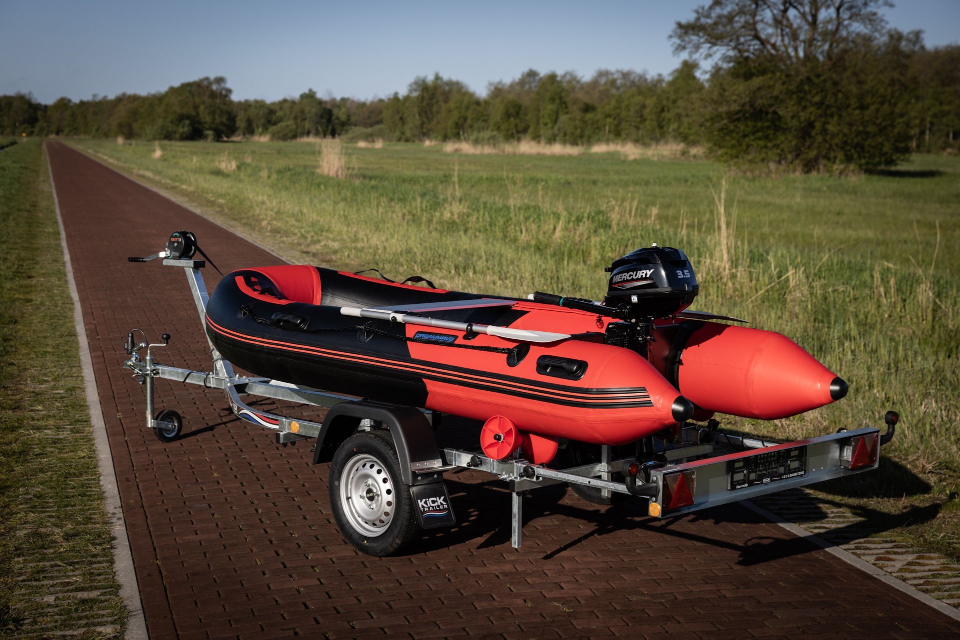 Een rood-zwarte boot staat op een trailer aan de kant van de weg.