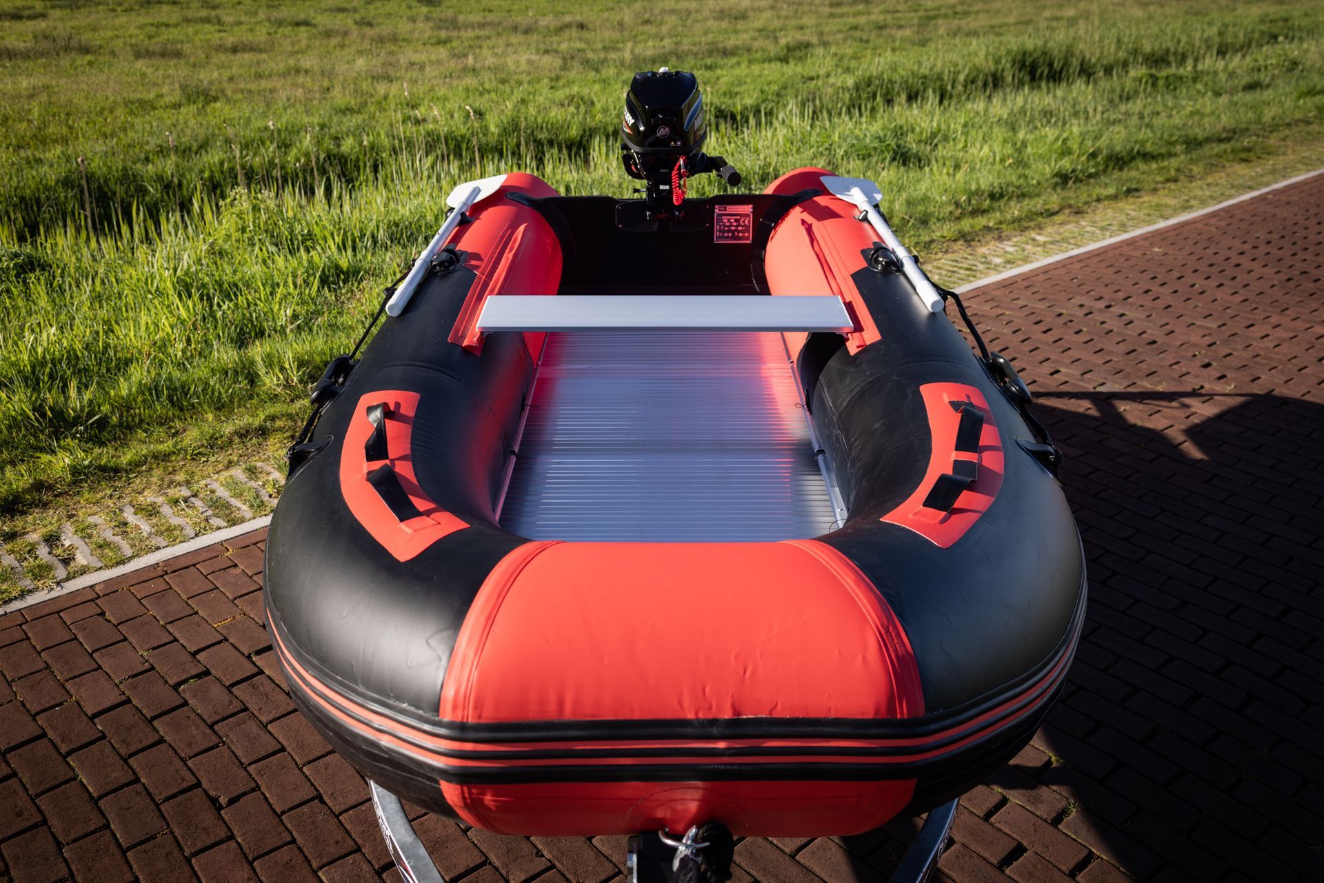 Een rode en zwarte opblaasbare boot staat geparkeerd op een stenen trottoir.