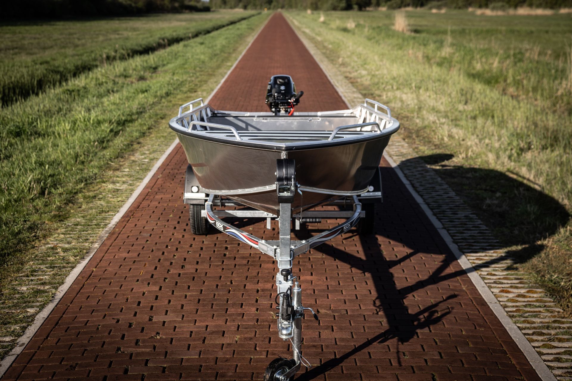 Een kleine boot staat op een trailer op een stenen weg.