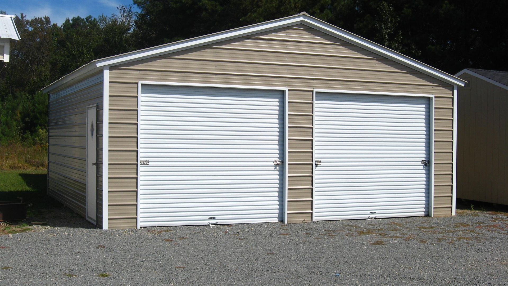 Tan two-car garage with white roll-up doors, light brown siding, and a gravel driveway.