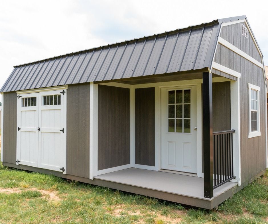 Gray shed with a porch and white doors on a grassy area.