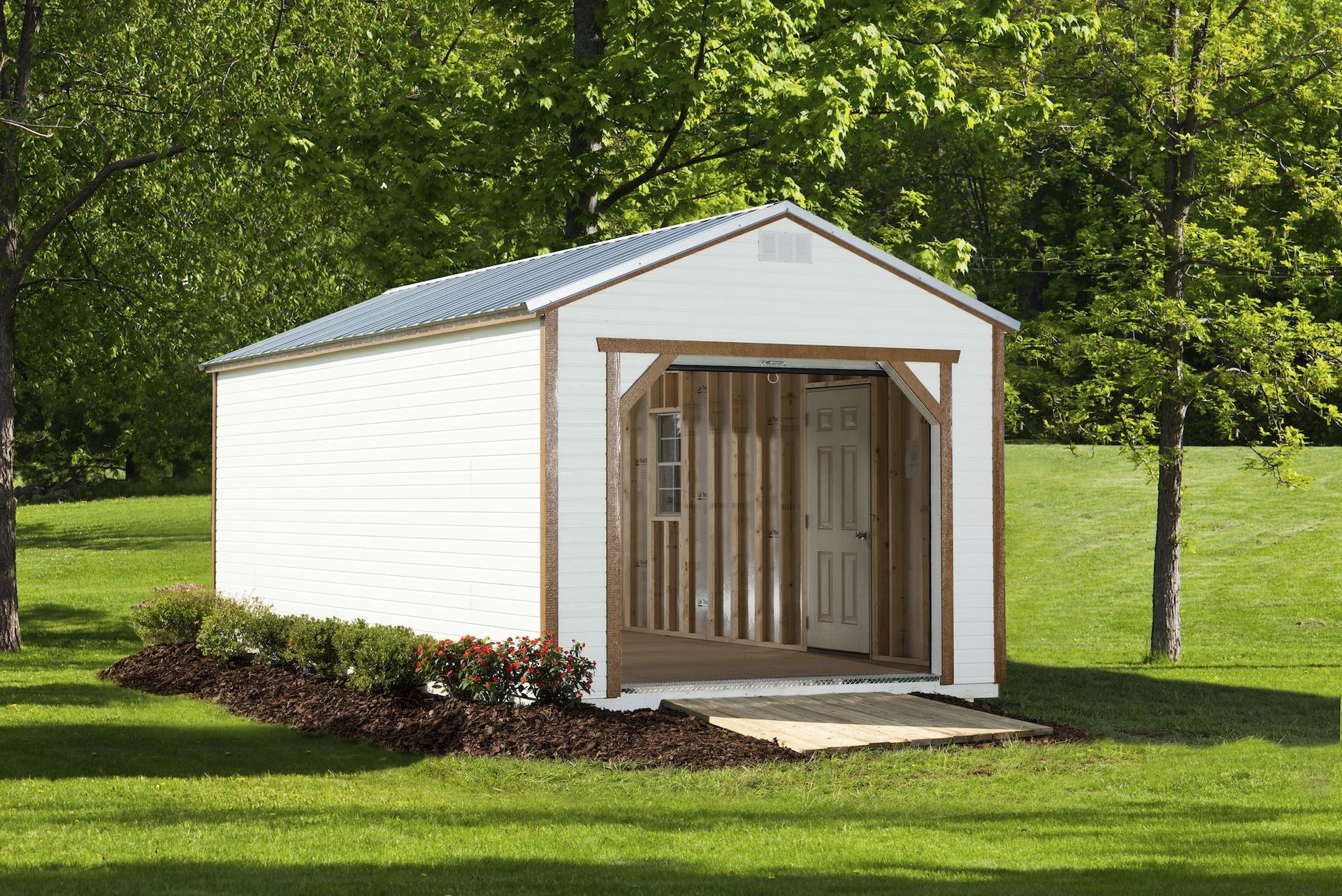 White shed with a small porch and open door, set in a grassy yard.