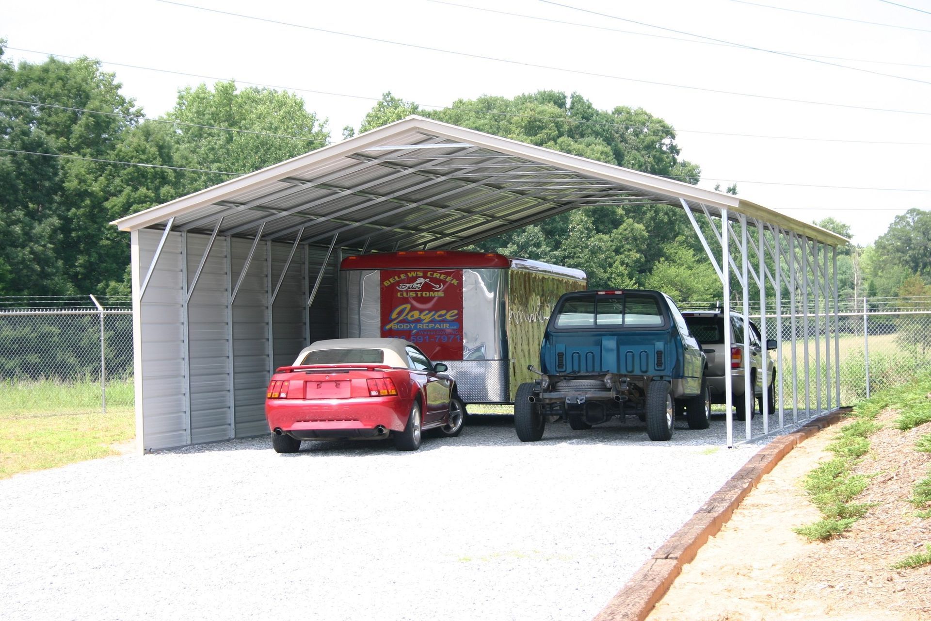 Metal carport sheltering vehicles of various types parked on gravel.