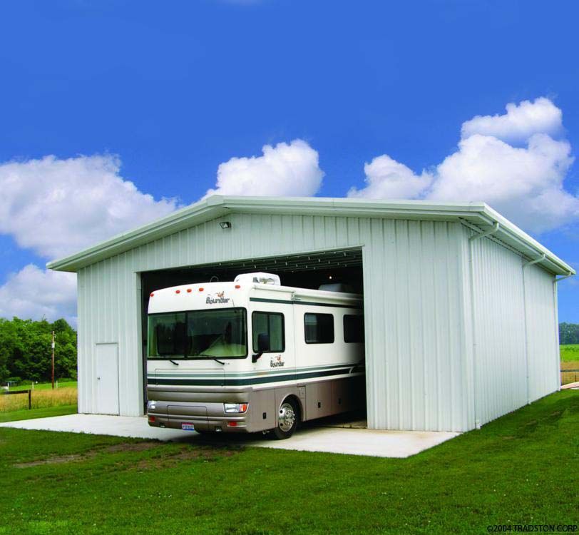 White RV in a large, white storage building on a grassy field under a blue sky with clouds.