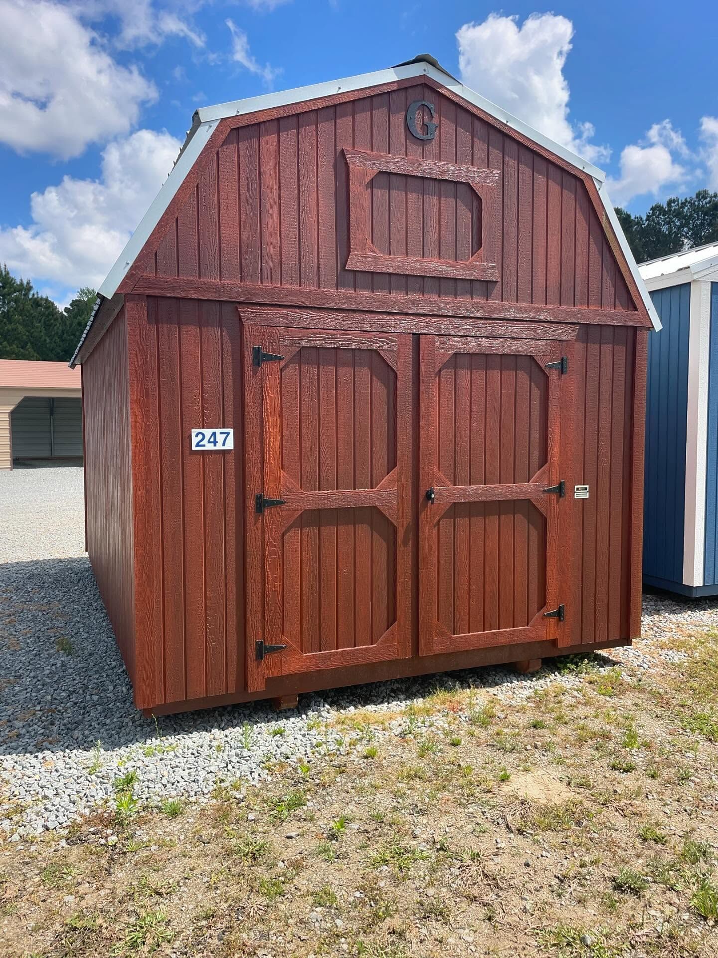 Red barn-style shed with double doors, white trim, and a loft window, set outdoors on gravel.