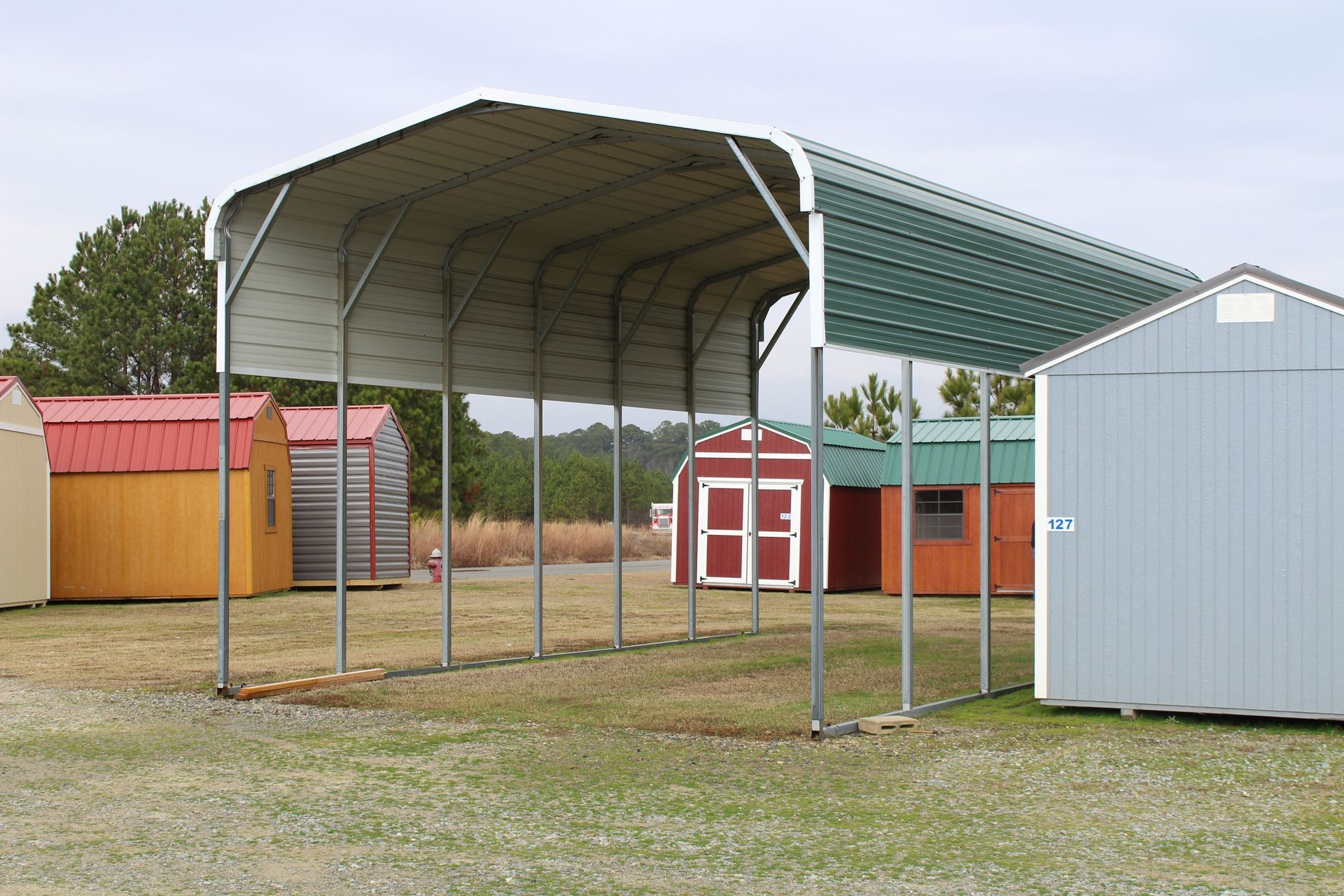 Metal carport with a green roof in front of colorful sheds.