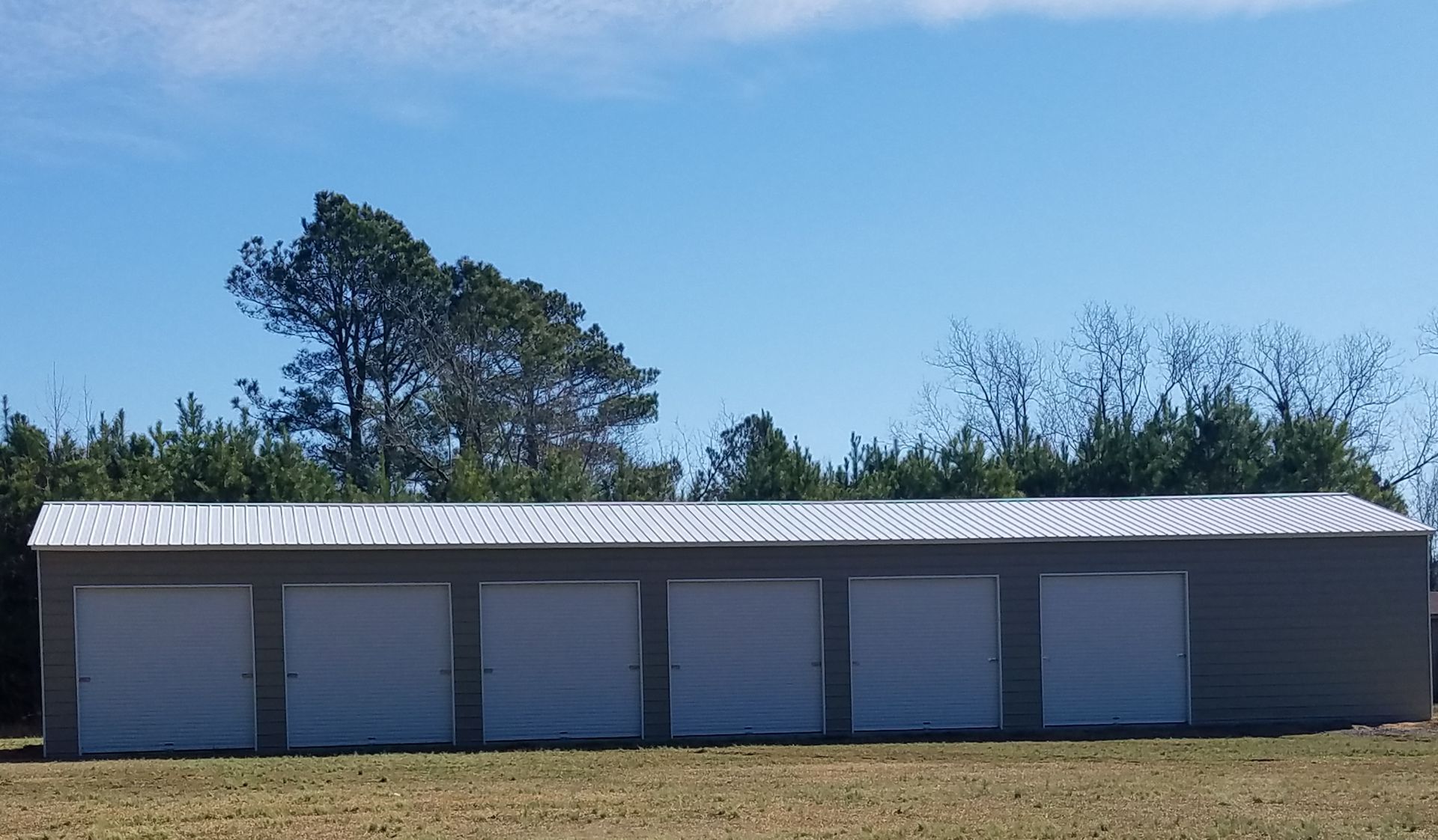 Six-unit storage building with white doors and corrugated metal roof, against a blue sky.