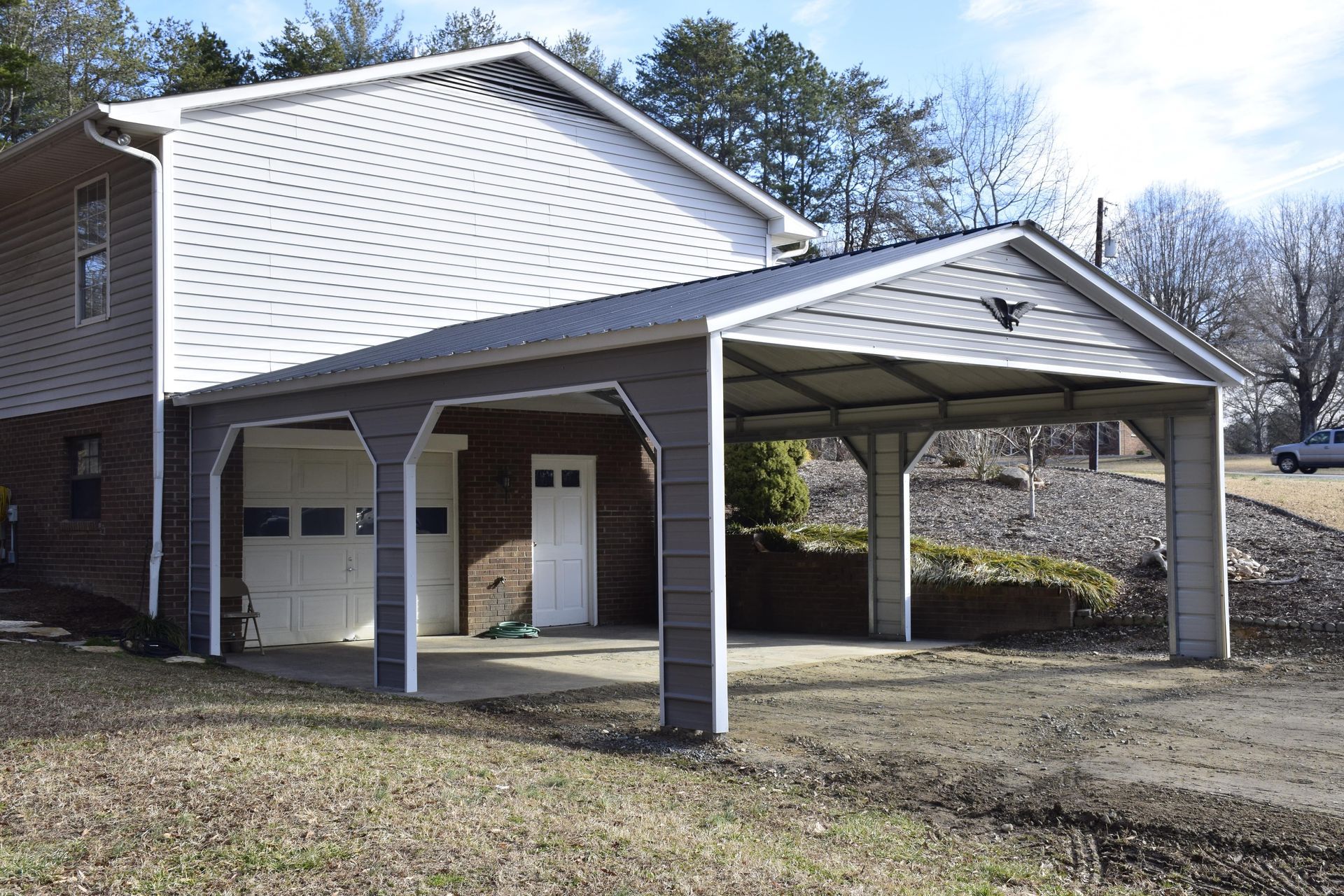 Gray carport attached to a two-story house, with a garage door and a white entry door.