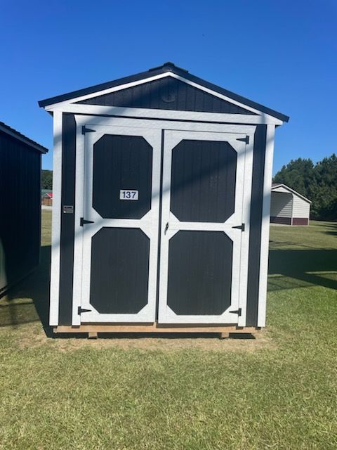 Brown shed with white trim, gray roof, door, and window on grassy ground.