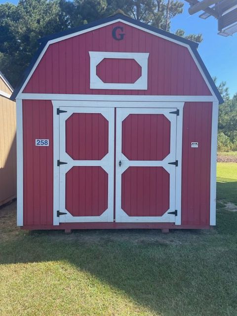 Gray shed with white trim, metal roof, two windows, and door on grass.