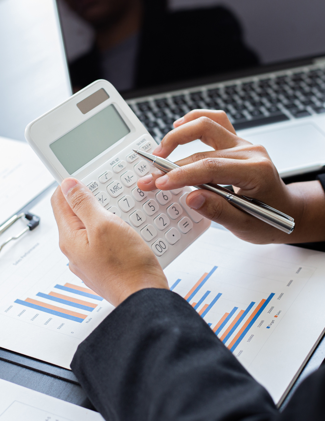 A person is using a calculator and a pen while sitting at a desk.