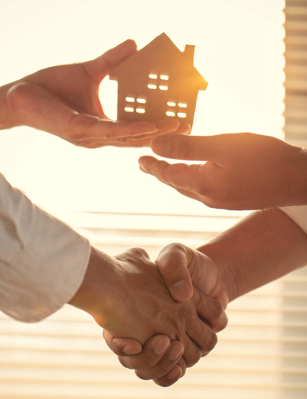 A person is shaking hands with another person while holding a model house.