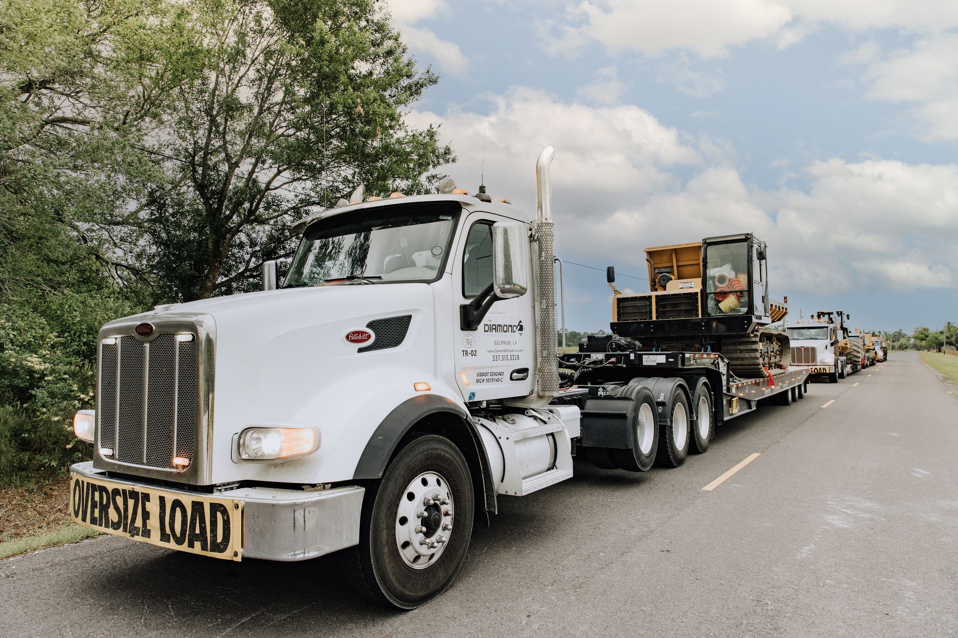 Three women standing on a job site with trees in background, wearing hard hats safety vests 