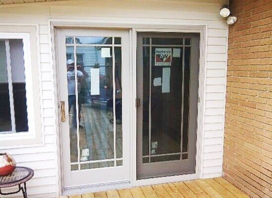 A sliding glass door is sitting on a wooden deck next to a brick wall.