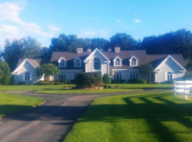 A large white house sits in the middle of a lush green field