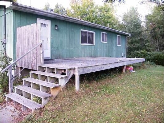 A green house with a deck and stairs in front of it.