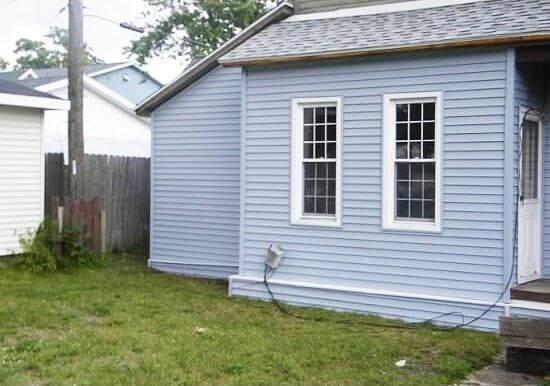A small blue house with two windows and a fence in the backyard.